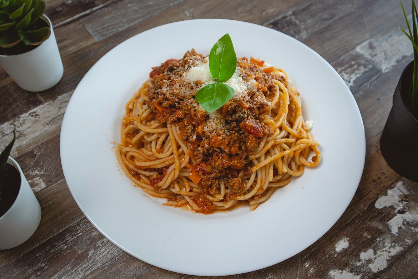 Teller Spaghetti mit stückiger roter Bolognese-Soße, geriebenem Käse und einem Basilikumblatt auf einem Holztisch